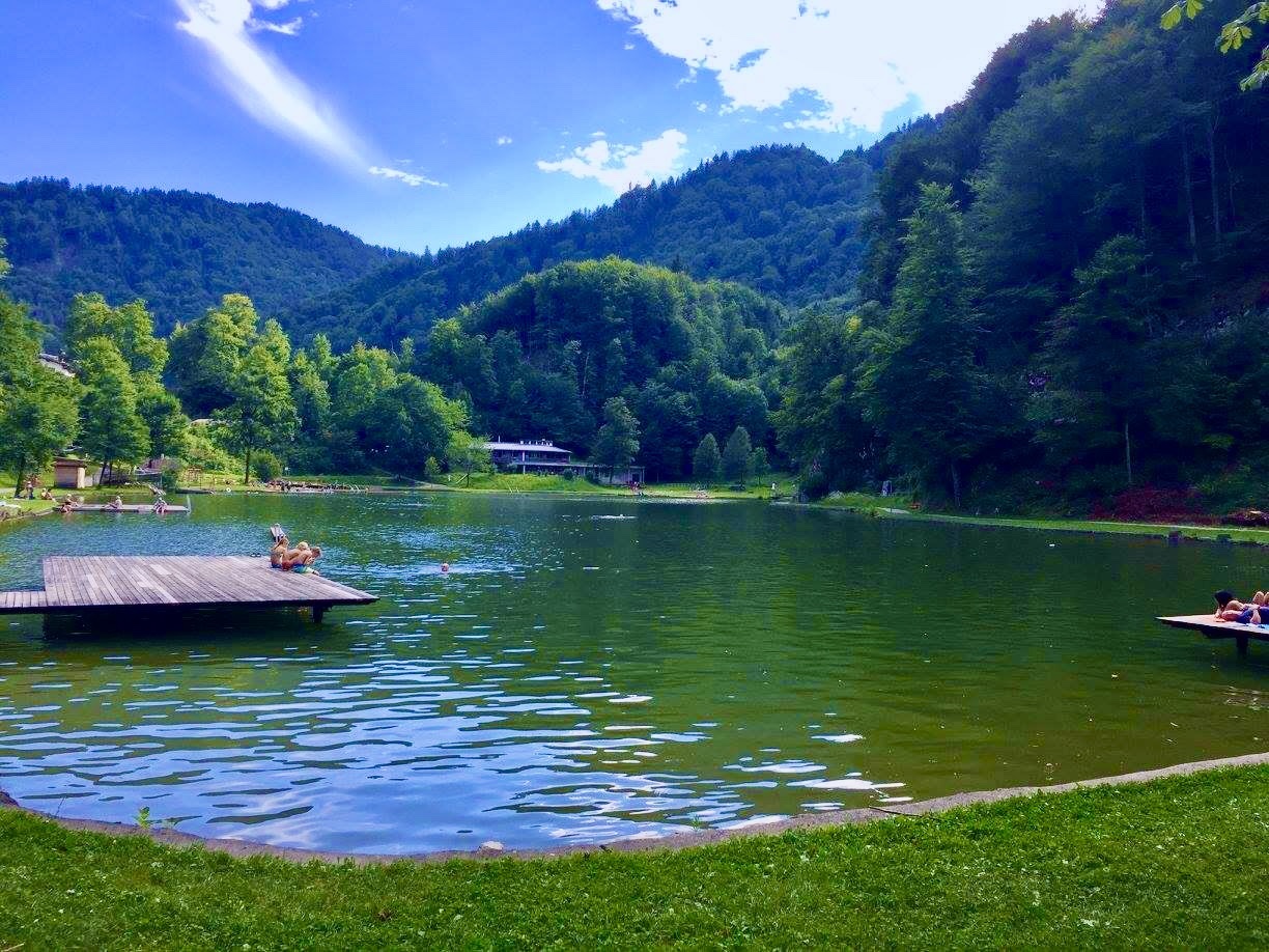 Swimmers and sunbathers on the docks of an alpine lake surrounded by forested hills